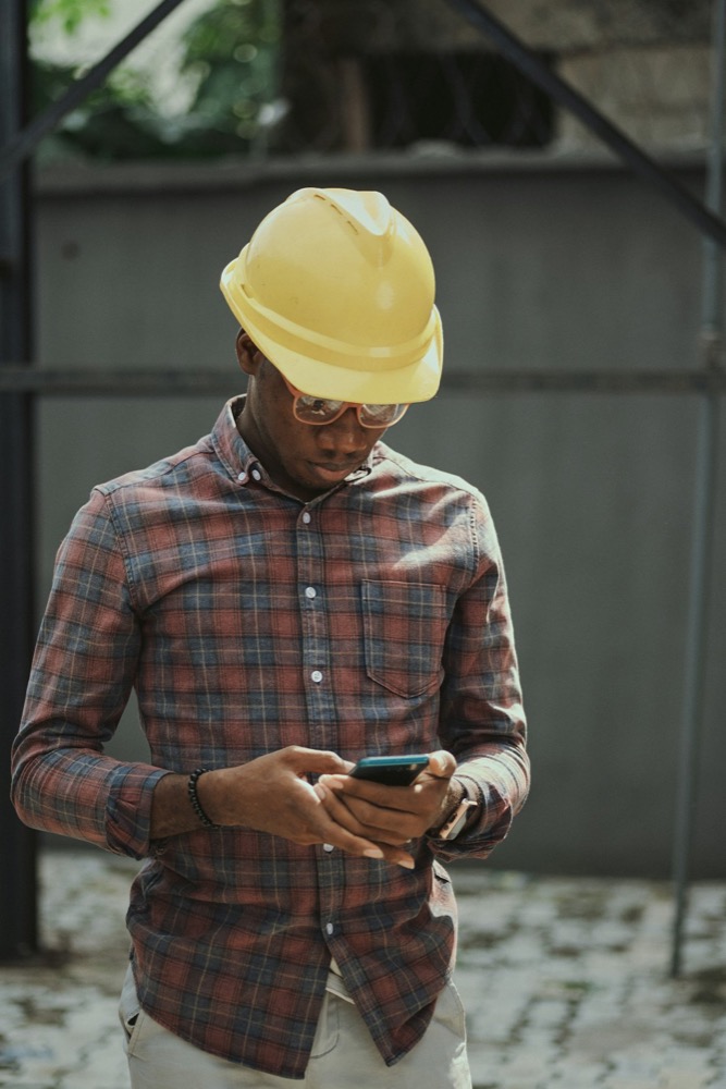 Technician in a hard hat checking a lead on his phone